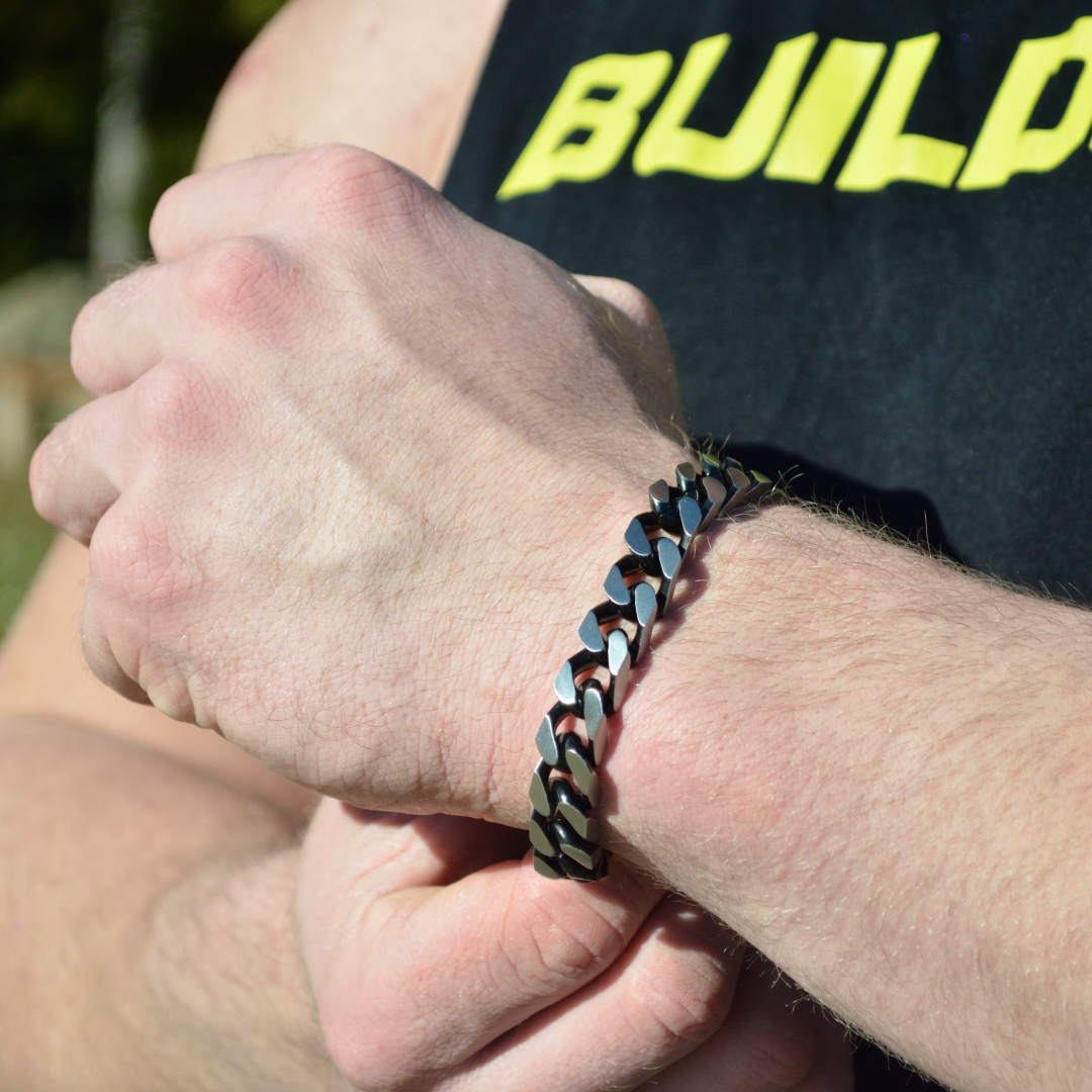 Armbandet bärs över svart t-shirt med gul text, handled i avslappnad position.#en:color_black,sv:farg_svart