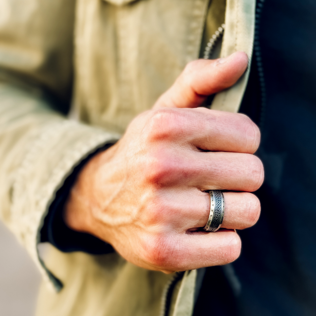 Närbild på man i beige jacka som visar Valhalla-ringen på handen.