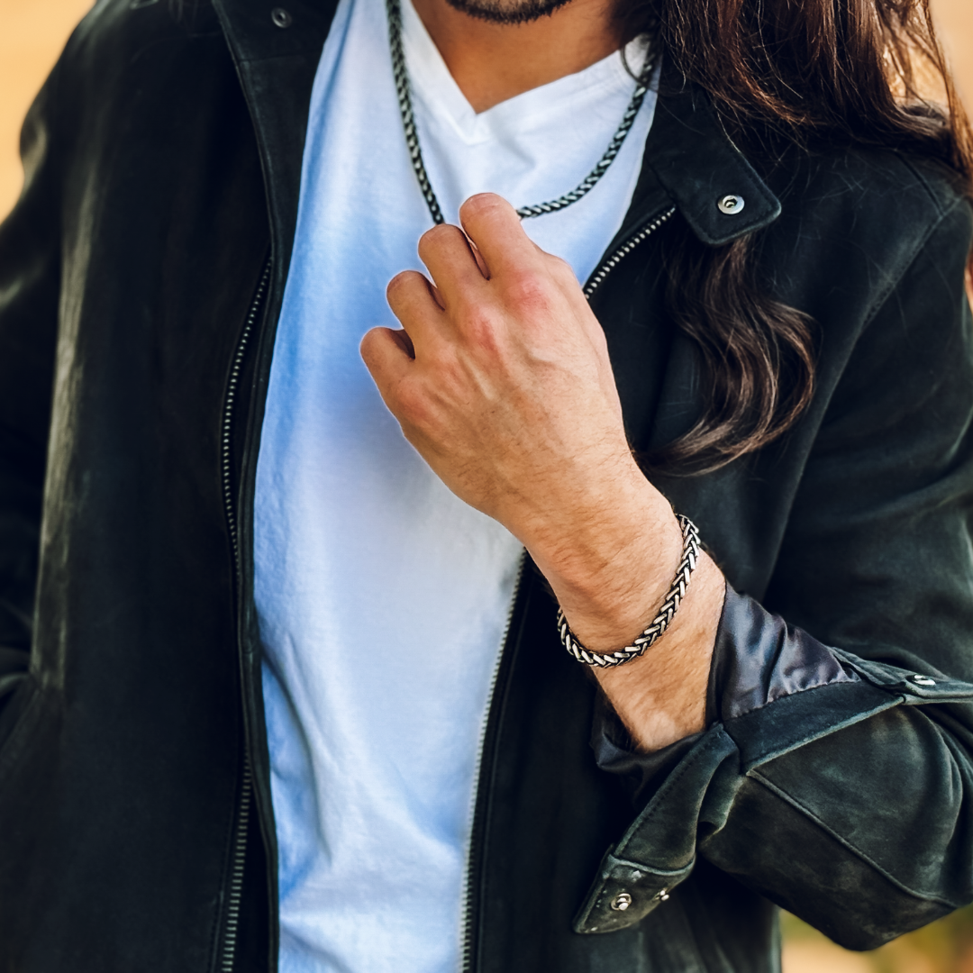 Man i läderjacka justerar kedjan, silverarmbandet kontrasterar mot vit t-shirt.#en:color_black,sv:farg_svart