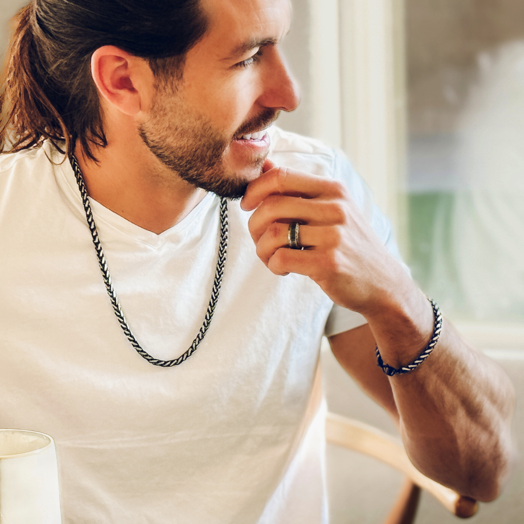 Avslappnad man dricker kaffe, kedjan fångar ljuset mot vit tröja – vardagslyx.#en:color_black,sv:farg_svart