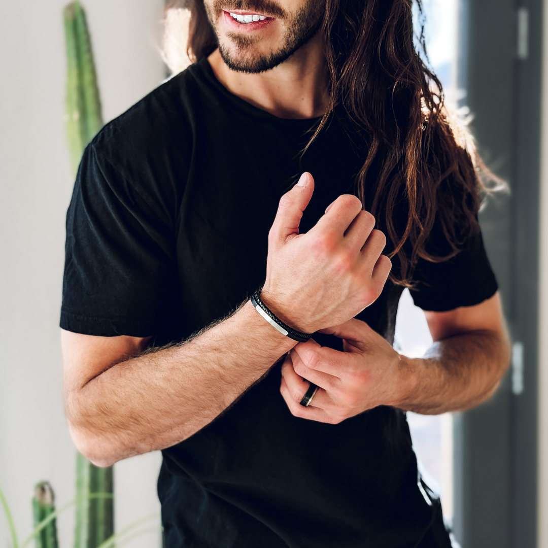 Man i svart t-shirt visar upp armbandet, enkel stil med självsäker attityd.#en:color_silver,sv:farg_silver