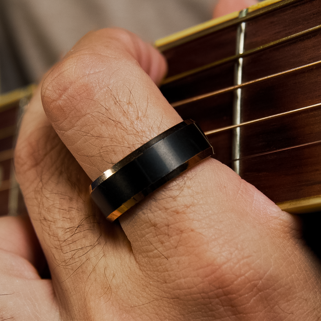 Hand spelar på gitarr, svart ring med guldkant syns tydligt mot träet.#en:color_black,sv:farg_svart
