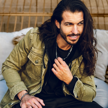 Sittande man bär både halsband och armband – modern stil med urban edge.