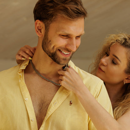 Man wearing a yellow shirt with a woman adjusting his necklace against a neutral background.
#en:color_silver,sv:farg_silver