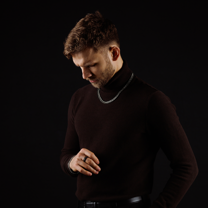 Profilbild i mörk miljö, kedjan reflekterar ljuset subtilt mot svart klädsel.