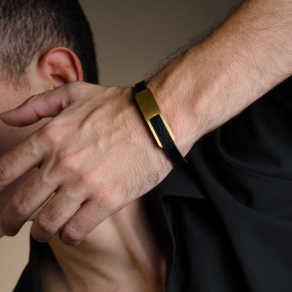 Ung man poserar i blå tröja, armbandet syns tydligt mot varm, beige bakgrund.
