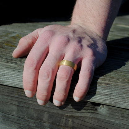 Ringen glänser i dagsljus när handen vilar mot träyta utomhus.
