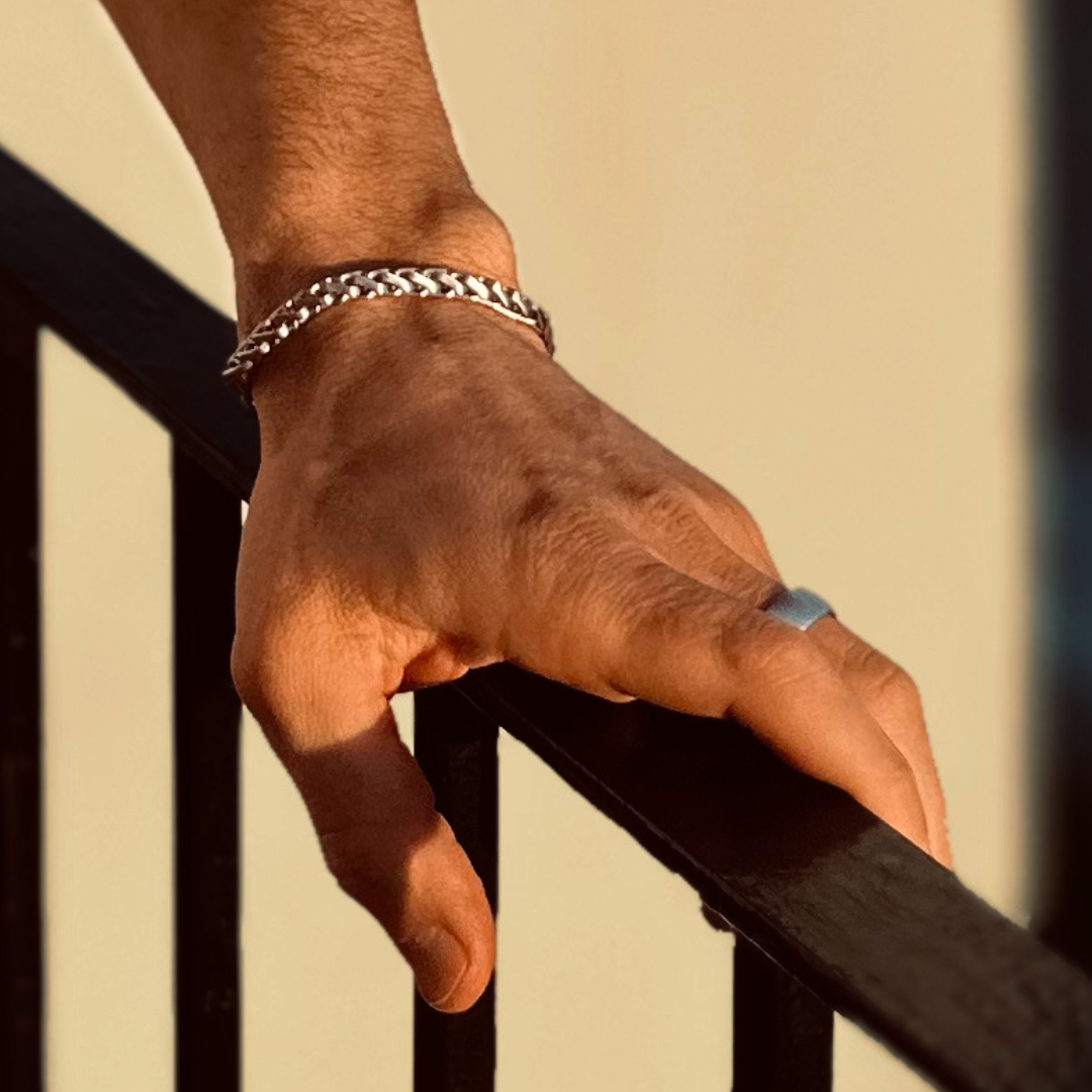 Man vilar handen mot räcke, armbandet glänser i gyllene dagsljus.#en:color_silver,sv:farg_silver