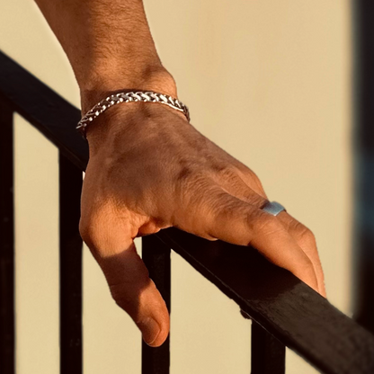 Man vilar handen mot räcke, armbandet glänser i gyllene dagsljus.