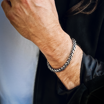Närbild på manlig handled med armbandet, svart jacka och naturligt dagsljus.