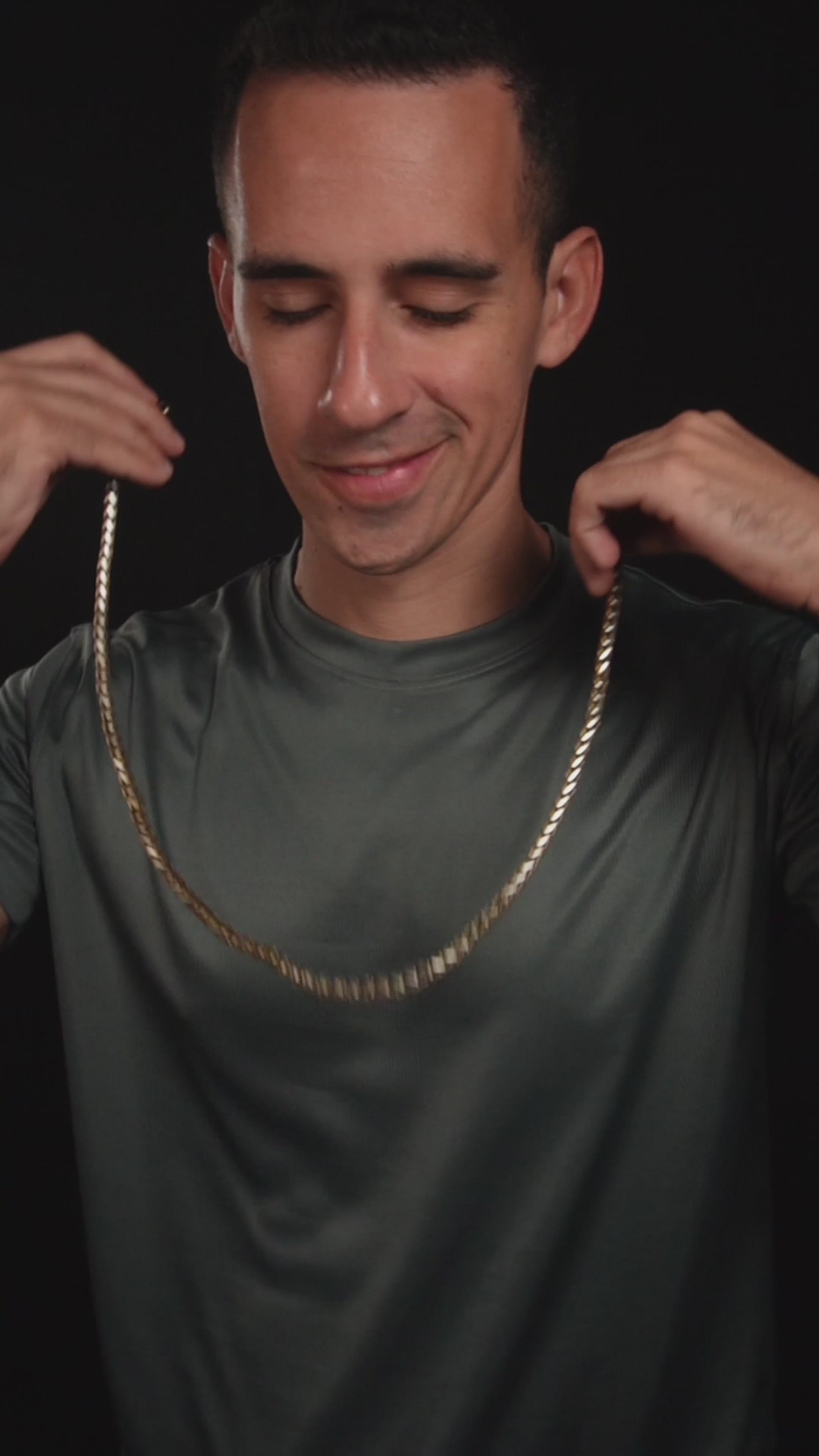 Videoikon över man som poserar med kedjan i spotlight, minimalistisk bakgrund.
